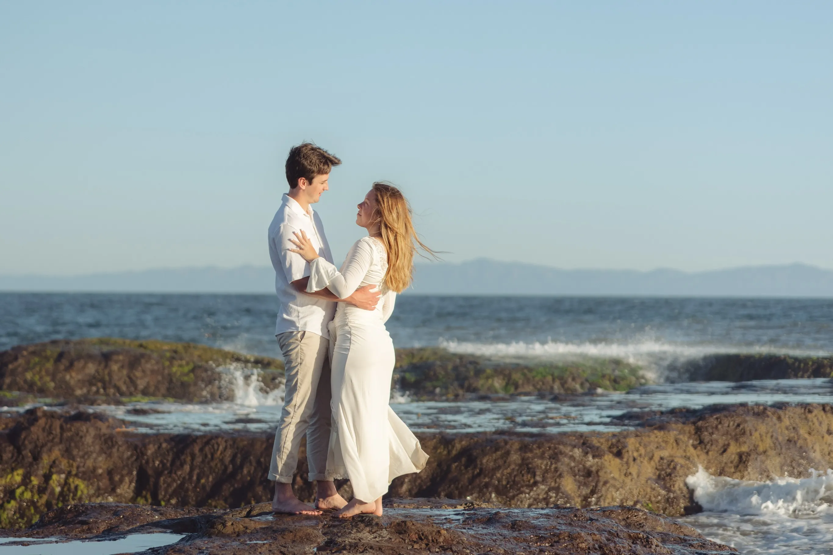 Couple standing on ocean rocks at sunset